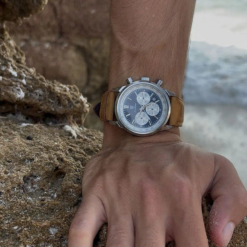 Sublime 41mm com pulseira de couro camel apoiado em uma pedra na praia
